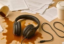 Hovedtelefonerne ligger i spildt kaffe på et skrivebord med dokumenter og to papkrus.