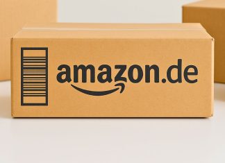 Amazon.de-pakken står centralt på et bord, omgivet af andre neutrale papkasser. Baggrunden er lys og enkel.